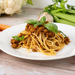 Spaghetti with Italian Style Vince on a white plate with vegetables in the background.  Healthy, quick, family meal using Vince’s hidden veggie mix, served with whole ingredients — perfect for picky eaters